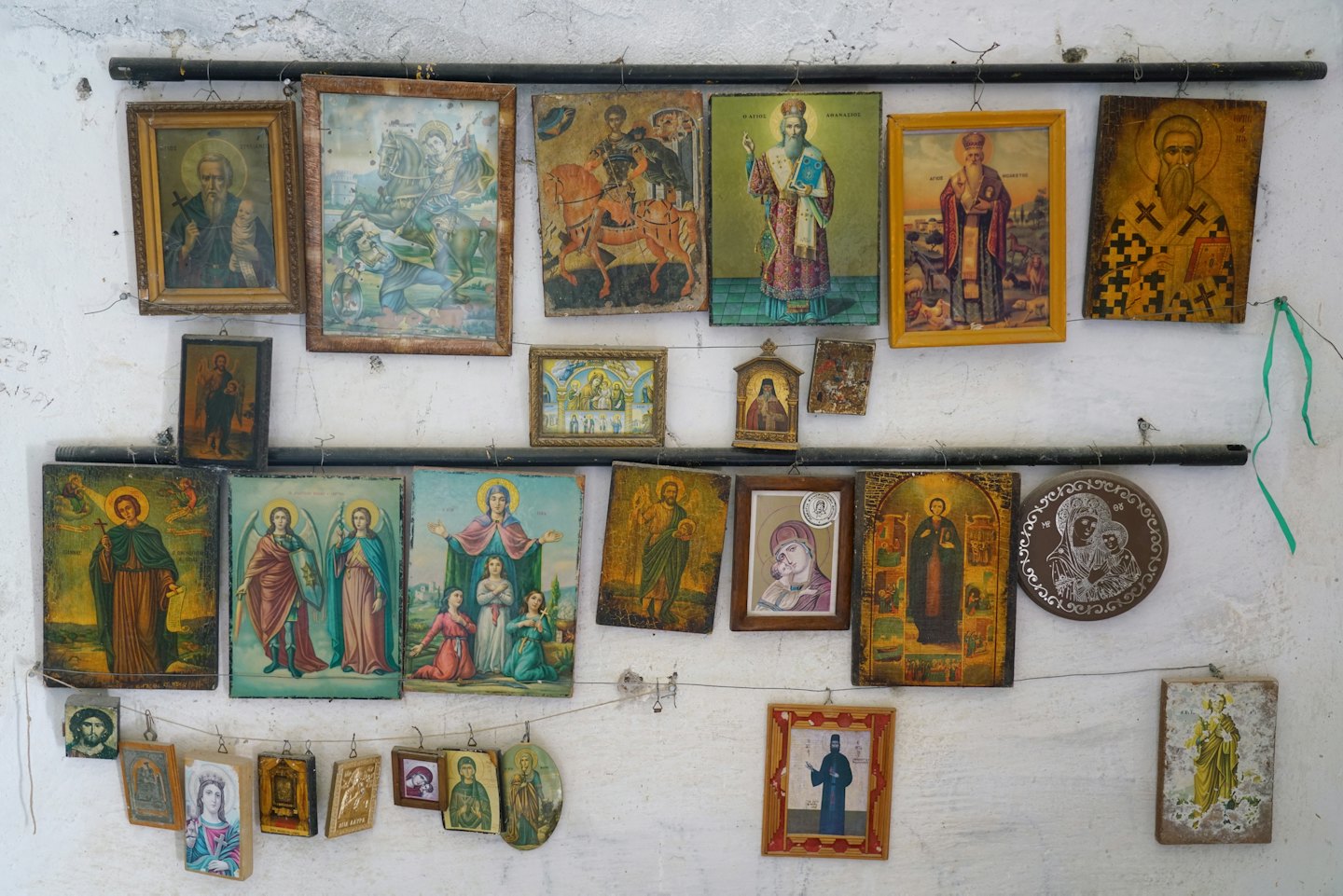 Religious icons and paintings hang densely on a white wall.