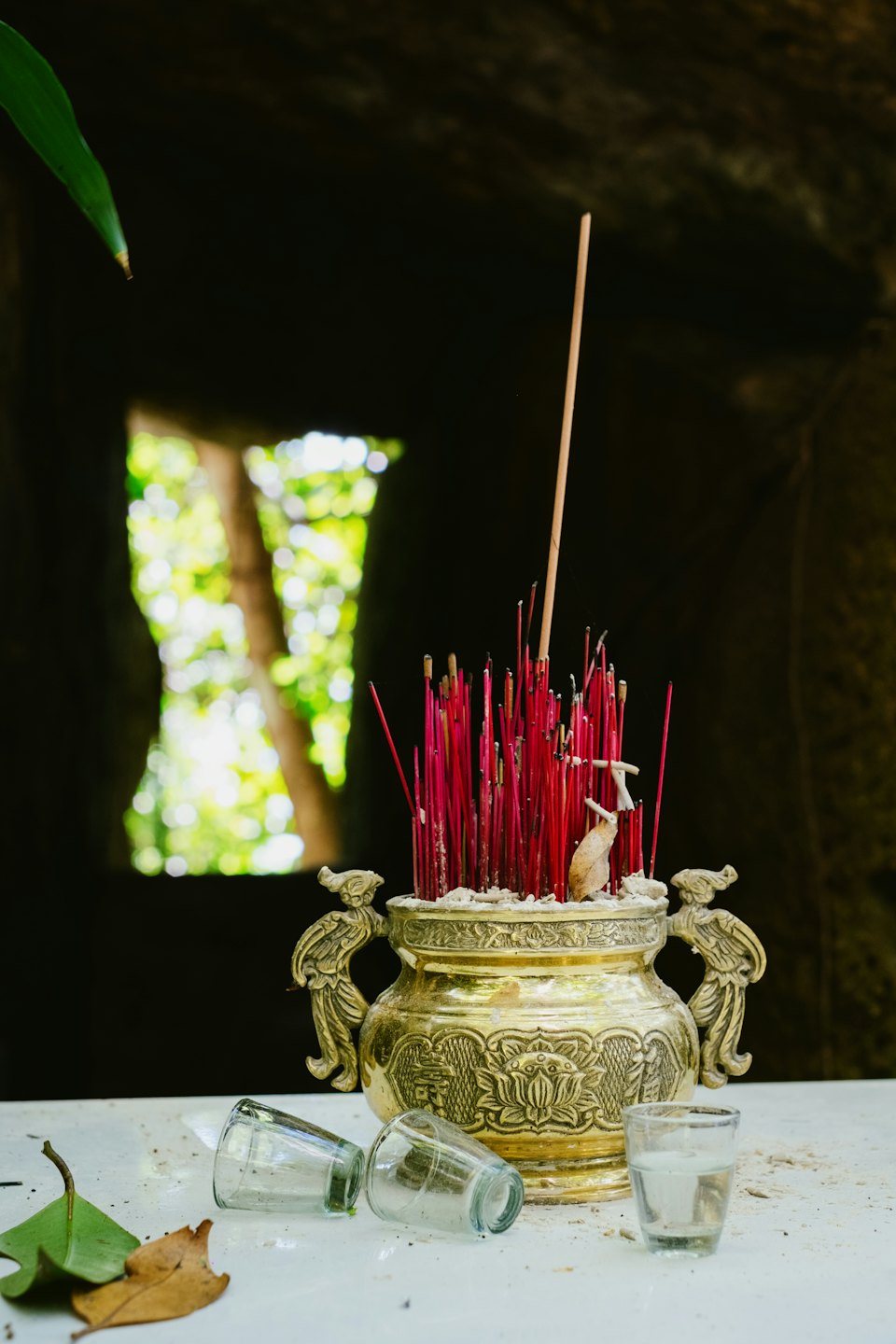 Brass incense burner with sticks and glass cups on a surface.